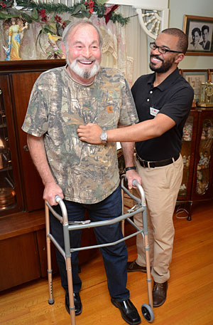 caregiver helping elderly man walk with a walker