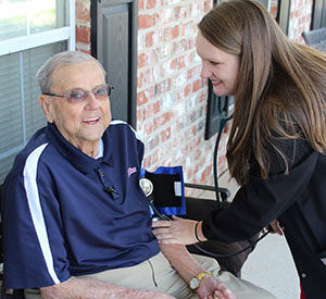 home health worker taking an elderly man's blood presure while sitting on a porch